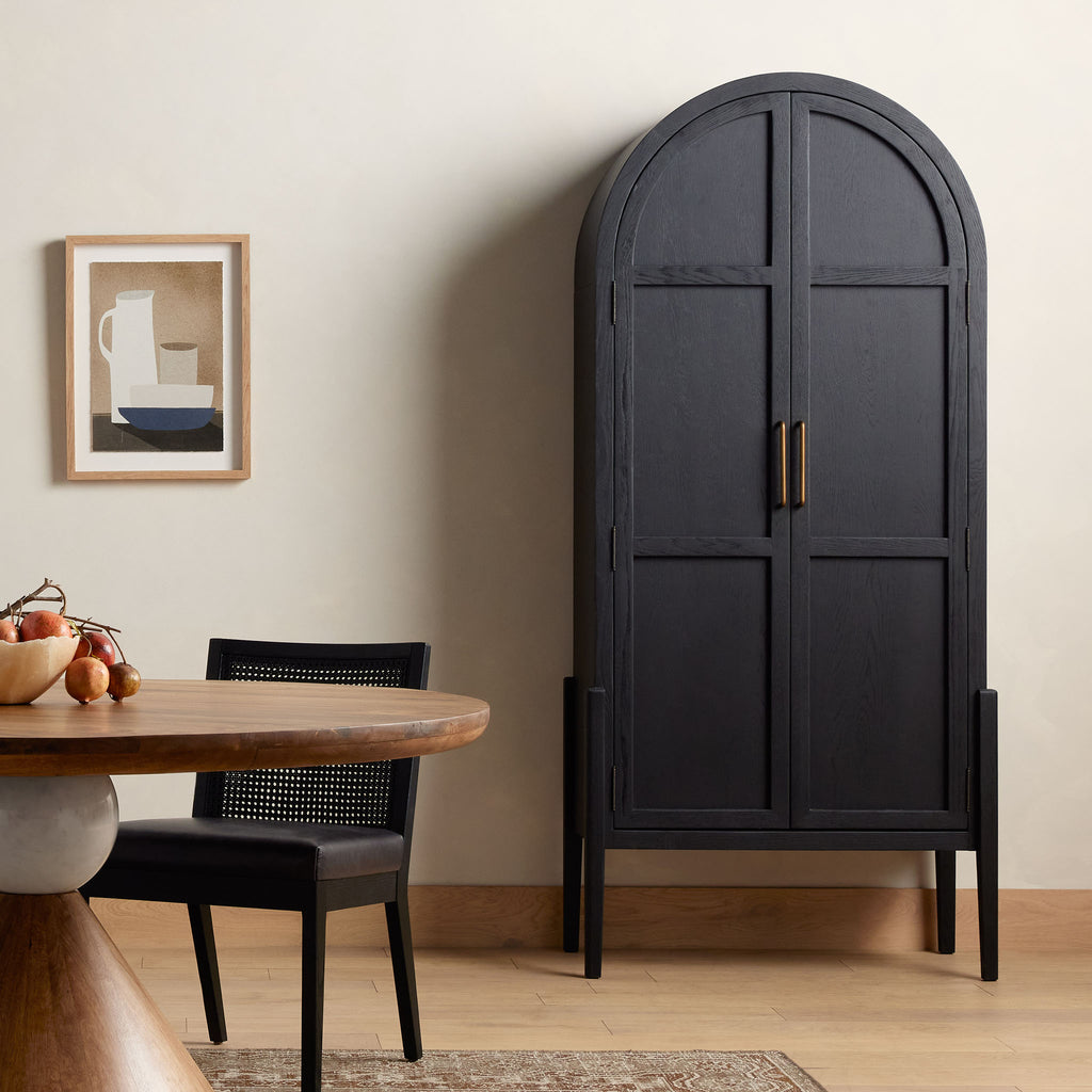Four hands furniture brand Tolle black cabinet with arched top and black wood stained interior in a dining room with wood floor and creme walls