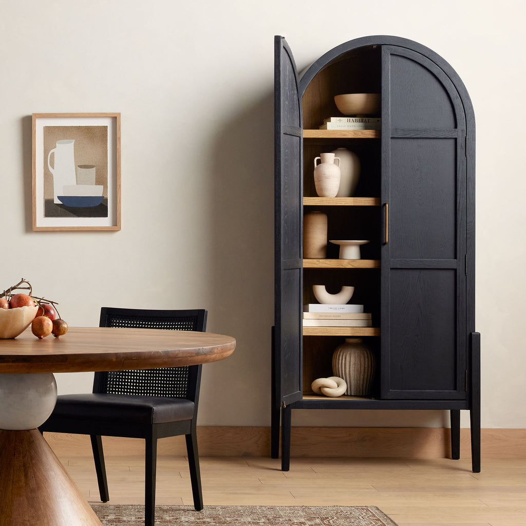 Four hands furniture brand Tolle black cabinet with arched top and black wood stained interior in a dining room with wood floor and creme walls