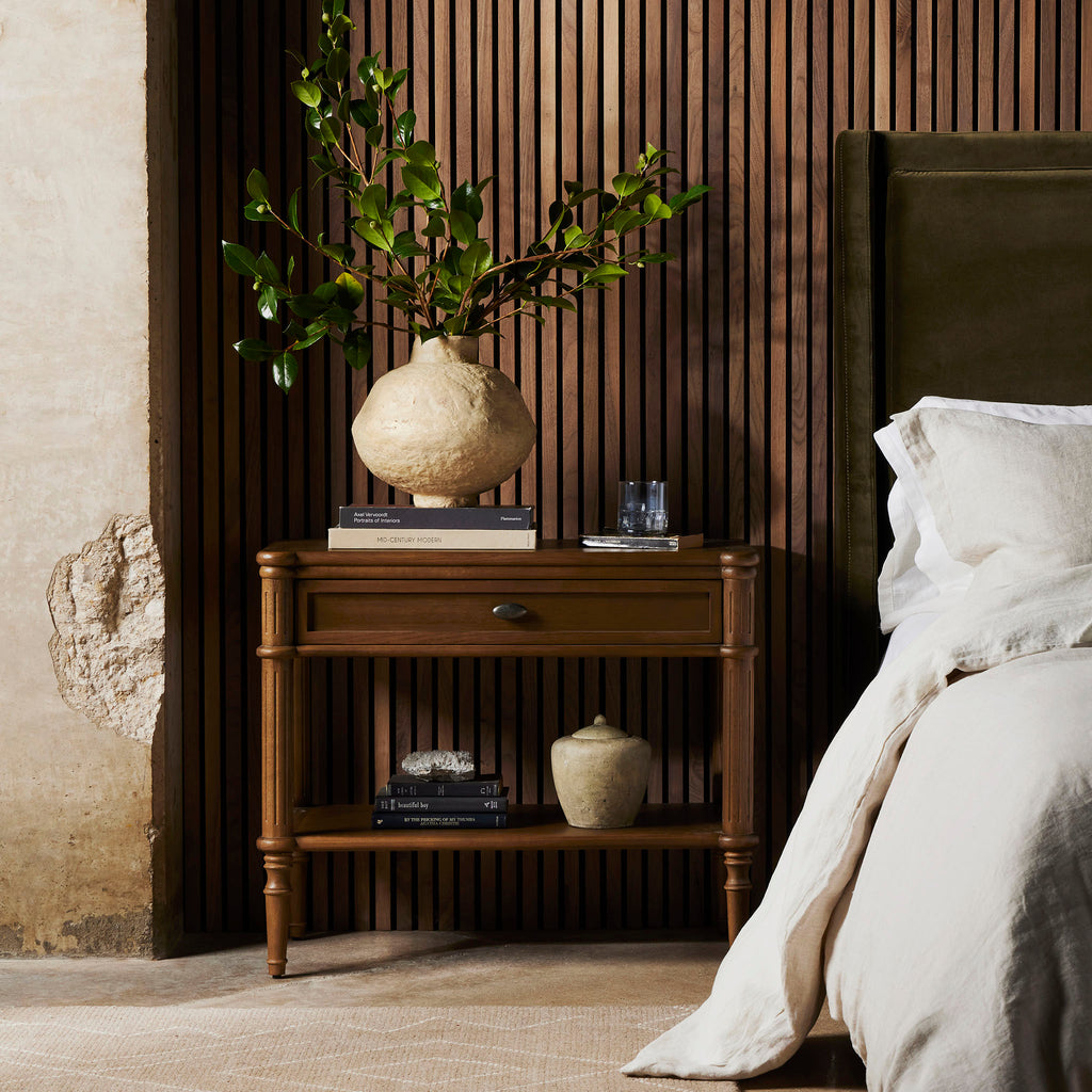 Oak 'Toulouse' nightstand with one drawer and shelf by four hands furniture in a bedroom with vase and books and wood wall 