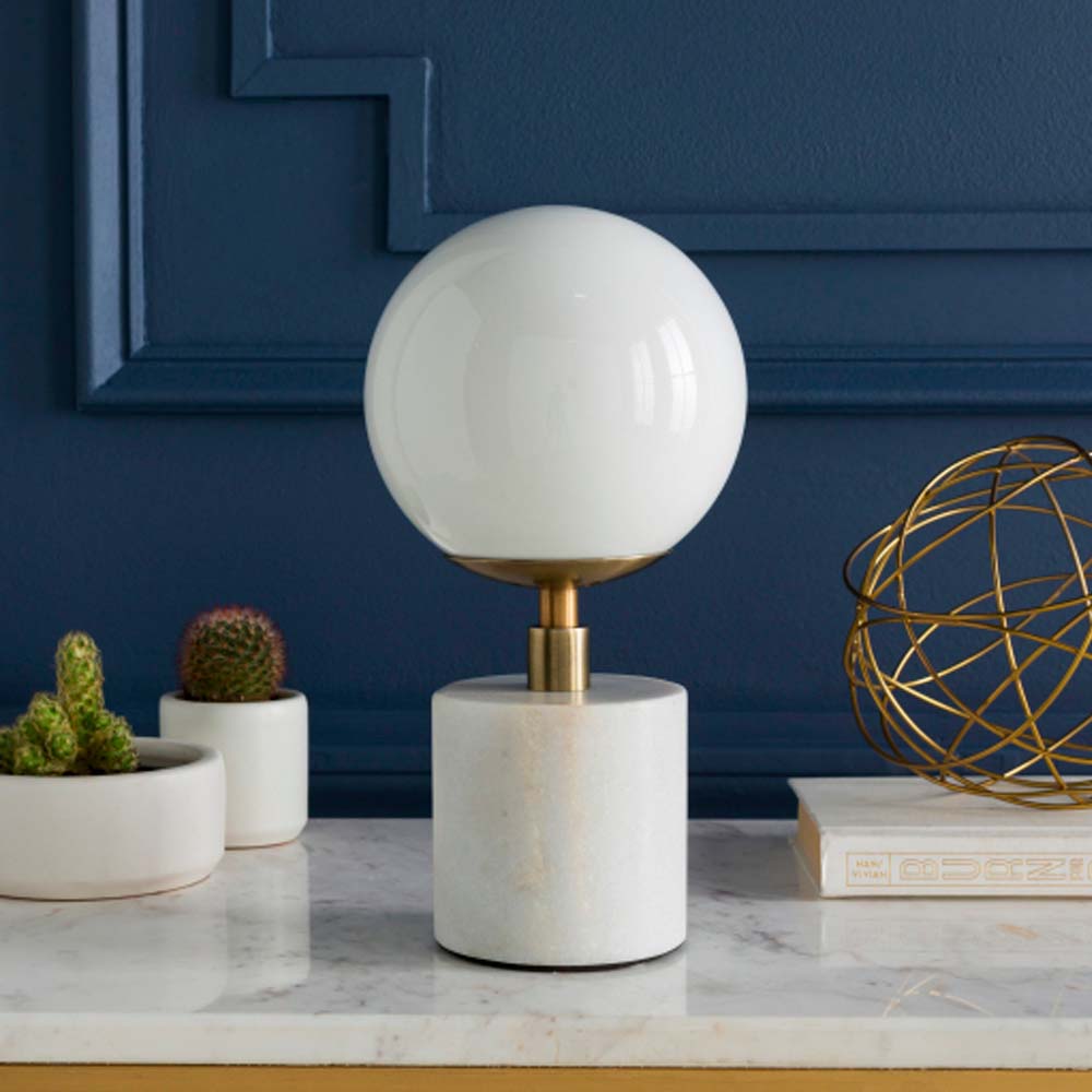 Surya brand Una marble table lamp with white milk glass globe shade and brass on a  marble surface with a blue background