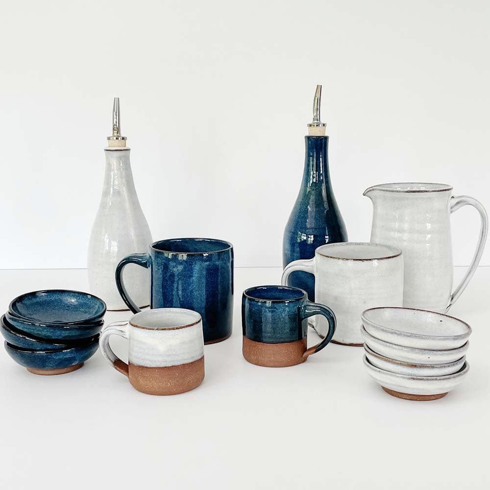 Collection of indigo and white Vermont made pottery mugs and bowls on a white background