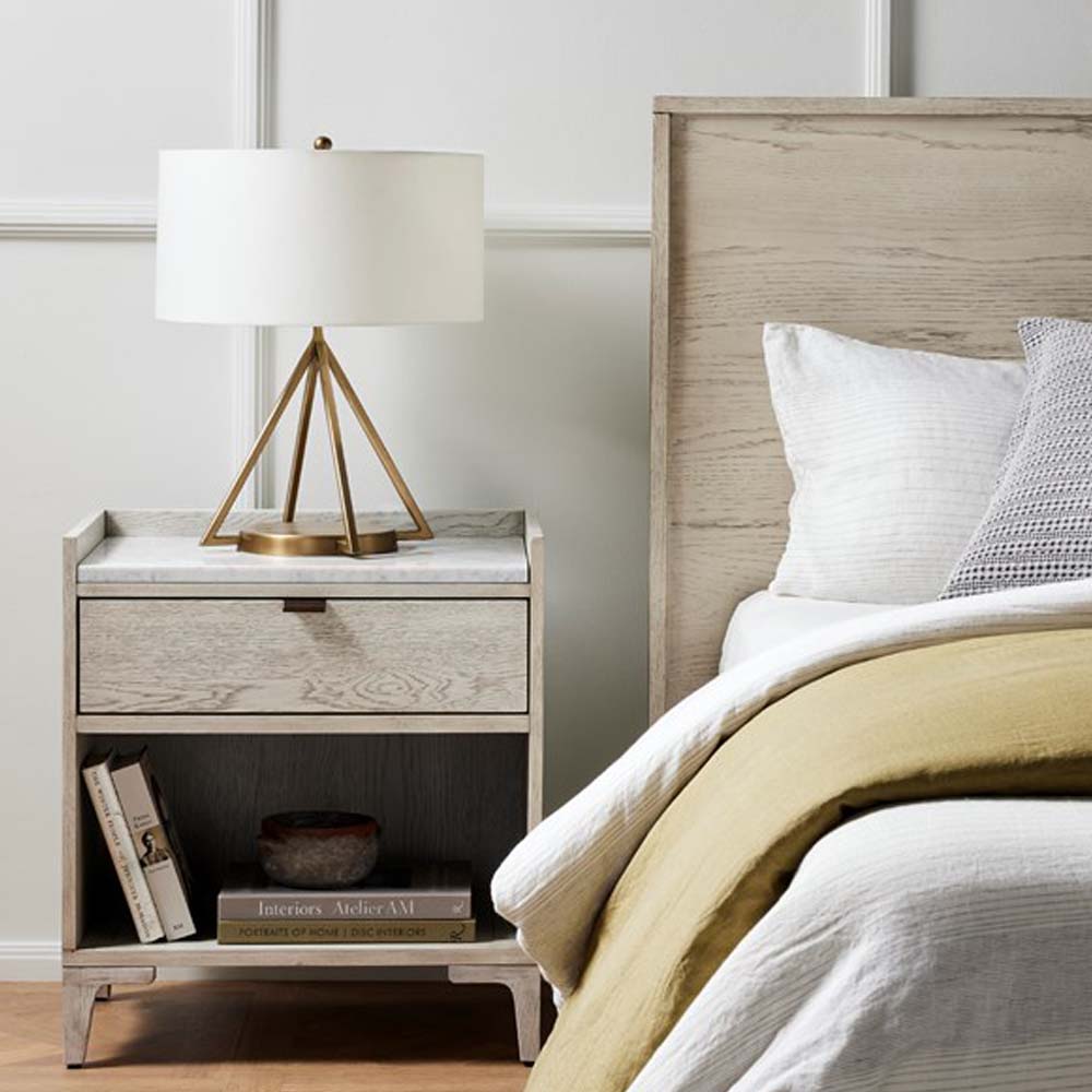 Whitewashed nightstand with drawer and marble beside bed with modern brass lamp