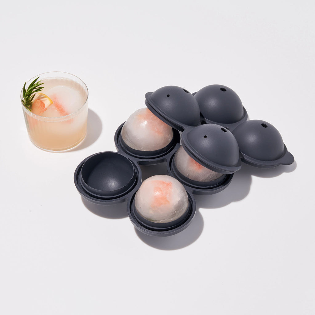 Silicone Sphere Ice Cocktail Tray by W & P on a white background next to a cocktail with ice cube