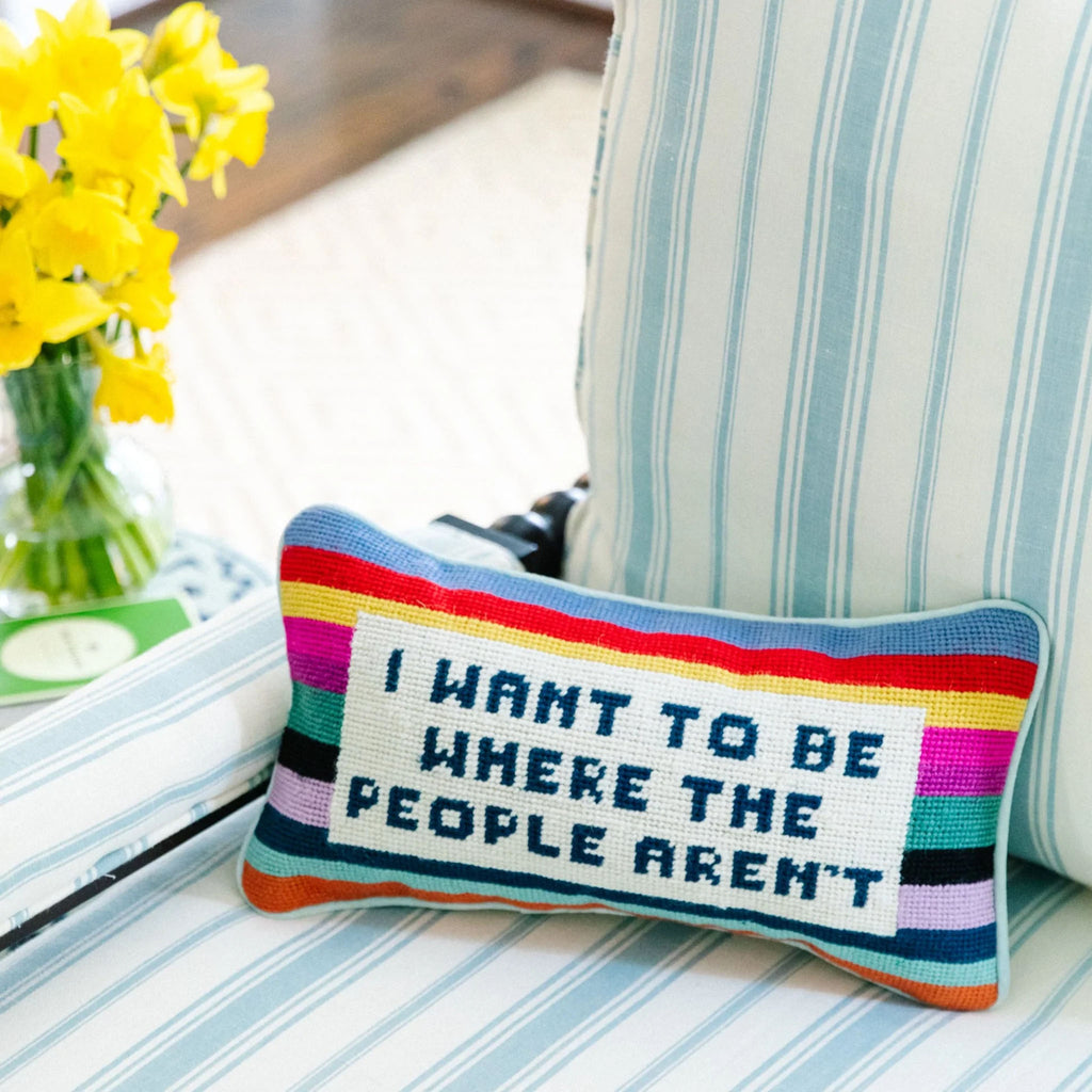 Needlepoint pillow with saying 'I want to be where the people aren't' on a blue and white striped chair