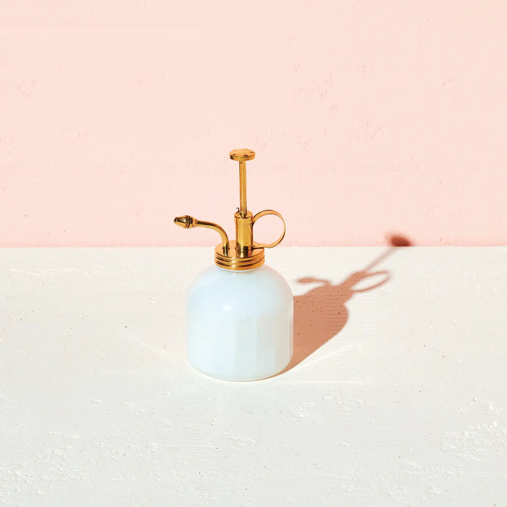 White glass and brass plant mister on a white surface