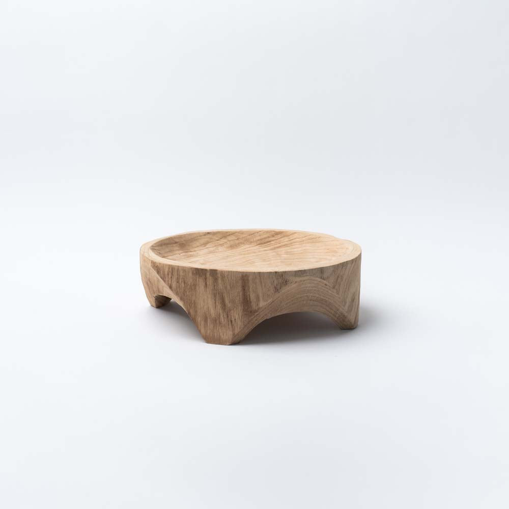 Shallow hand carved wood bowl with four feet on a white background