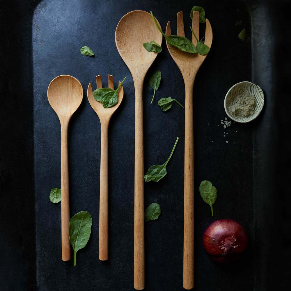 Beechwood salad server on a black surface with salad leaves strewn about 
