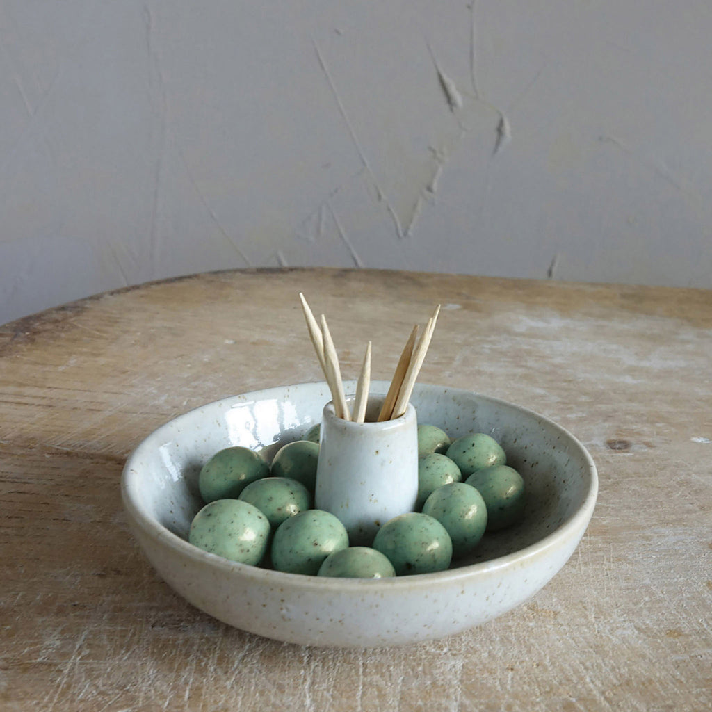Stoneware holder with olives and tool picks on a wood surface