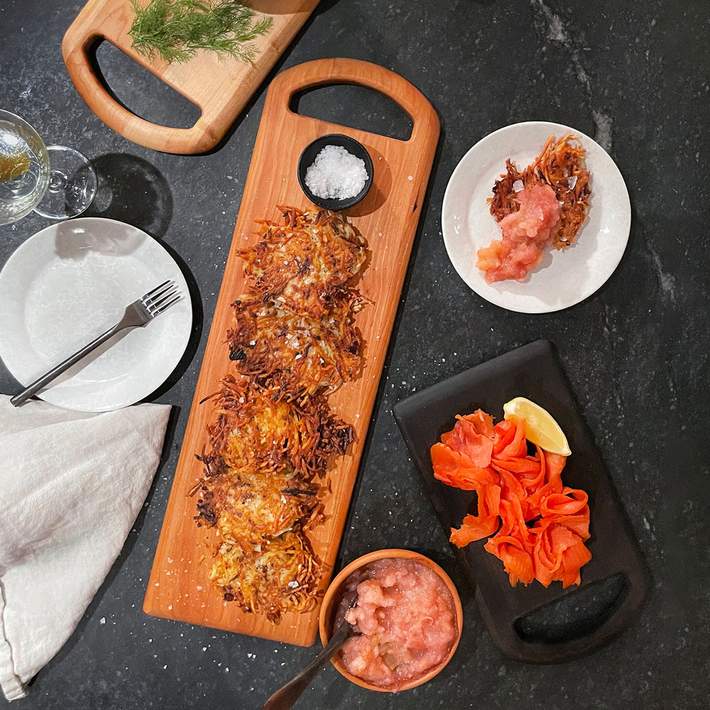 JK Adams long cherry serving board with rounded handle on a counter with appetizers