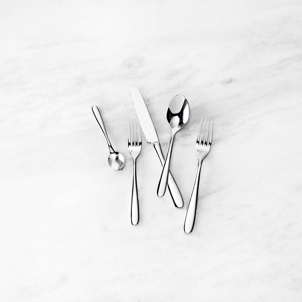 Stainless steel place setting with two forks a knife and two spoons with rounded handles on a marble surface