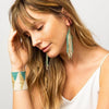 Model wearing Ink and alloy brand wide beaded stretch bracelet in gold and teal on a white background
